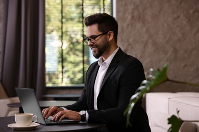 Happy young man with glasses working on laptop at table in office