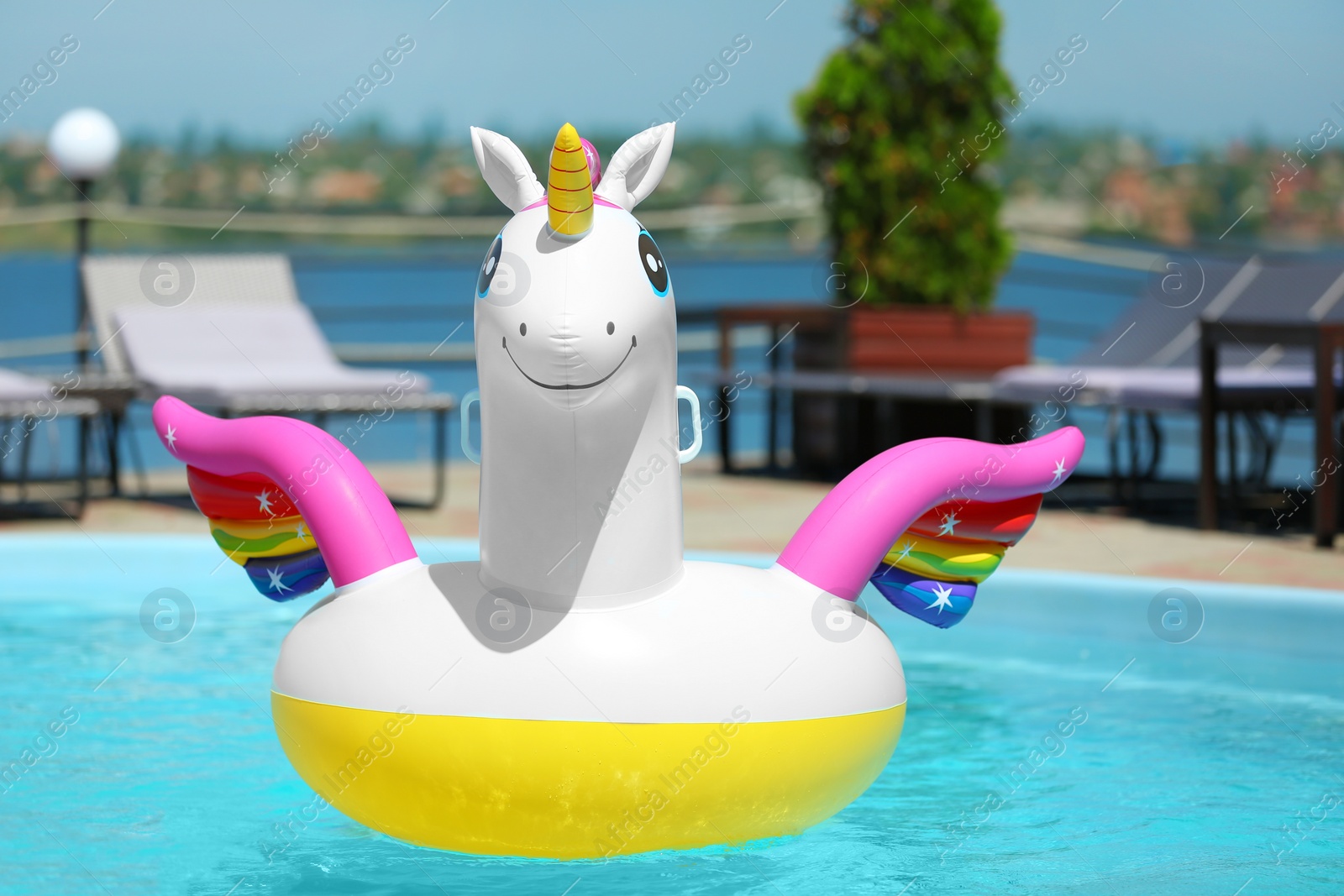 Photo of Funny inflatable unicorn ring floating in swimming pool on sunny day, outdoors