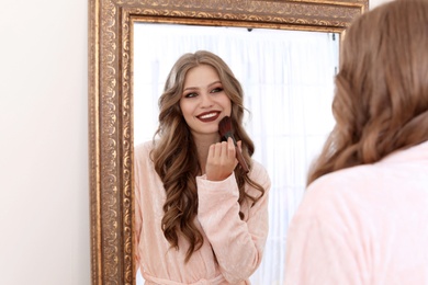 Photo of Young woman applying makeup near mirror in dressing room