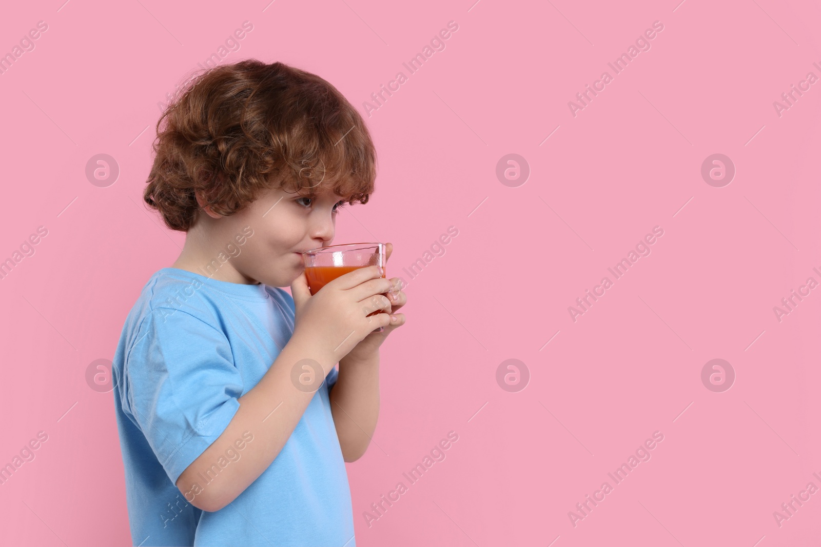 Photo of Cute little boy drinking fresh juice on pink background, space for text