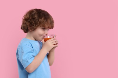 Photo of Cute little boy drinking fresh juice on pink background, space for text