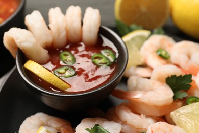 Photo of Tasty boiled shrimps with cocktail sauce, chili, parsley and lemon on table, closeup