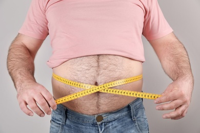 Photo of Overweight man with large belly and measuring tape on color background, closeup