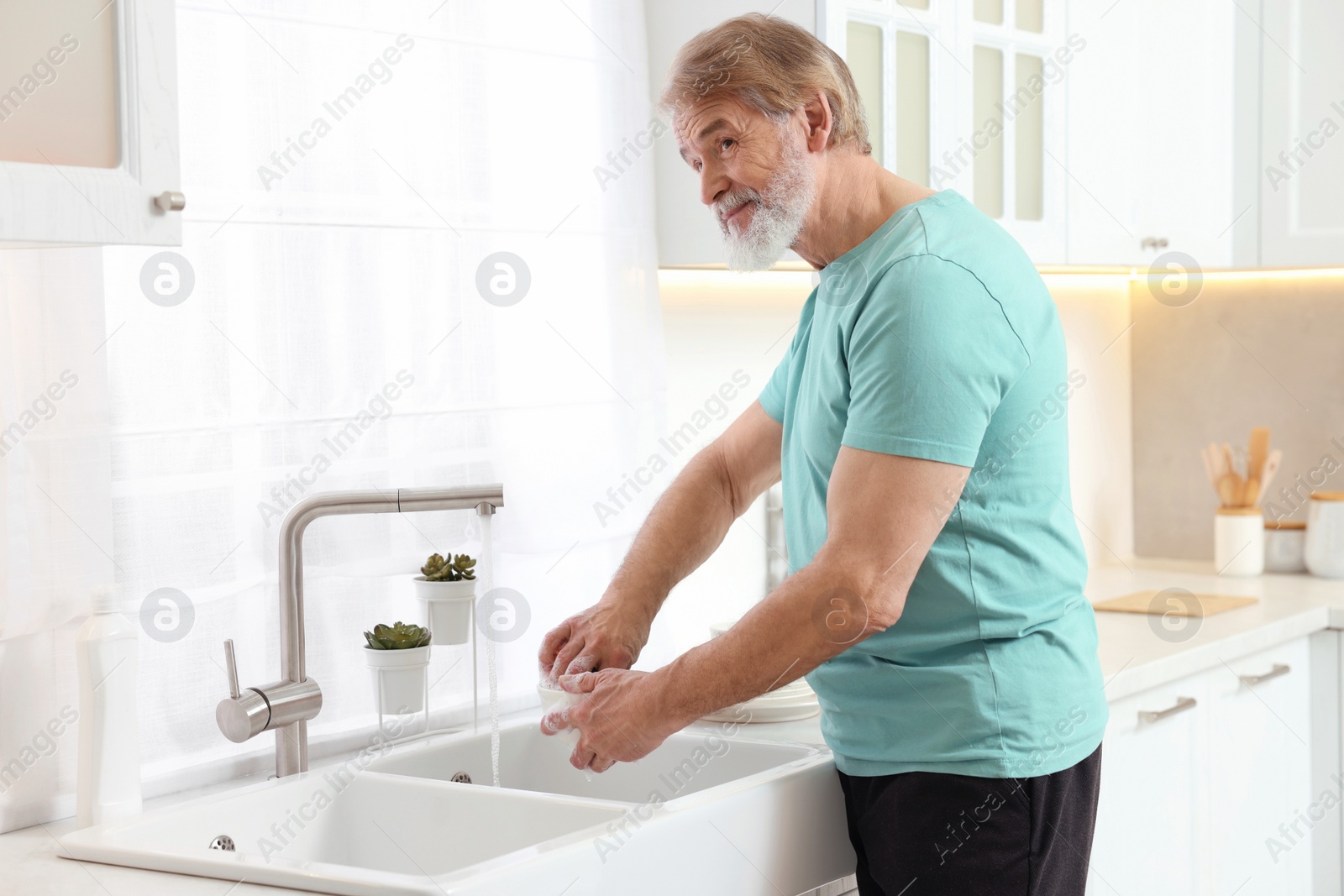 Photo of Senior man washing bowl above sink in kitchen