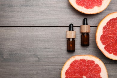 Photo of Bottles of citrus essential oil and grapefruit slices on wooden table, flat lay. Space for text