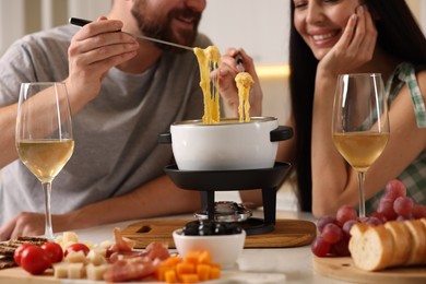 Couple enjoying cheese fondue during romantic date indoors, closeup