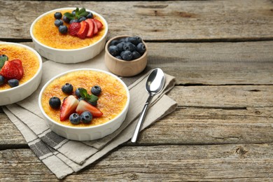 Delicious creme brulee with berries and mint in bowls on wooden table. Space for text