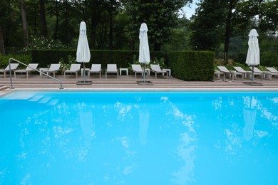 Photo of Many sunbeds and umbrellas near outdoor swimming pool