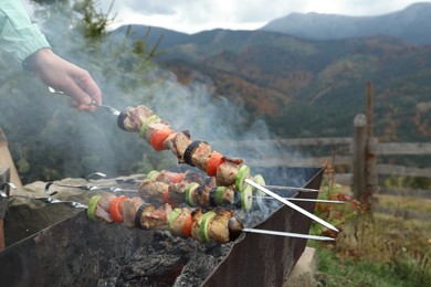 Photo of Woman cooking meat and vegetables on brazier against mountain landscape, closeup