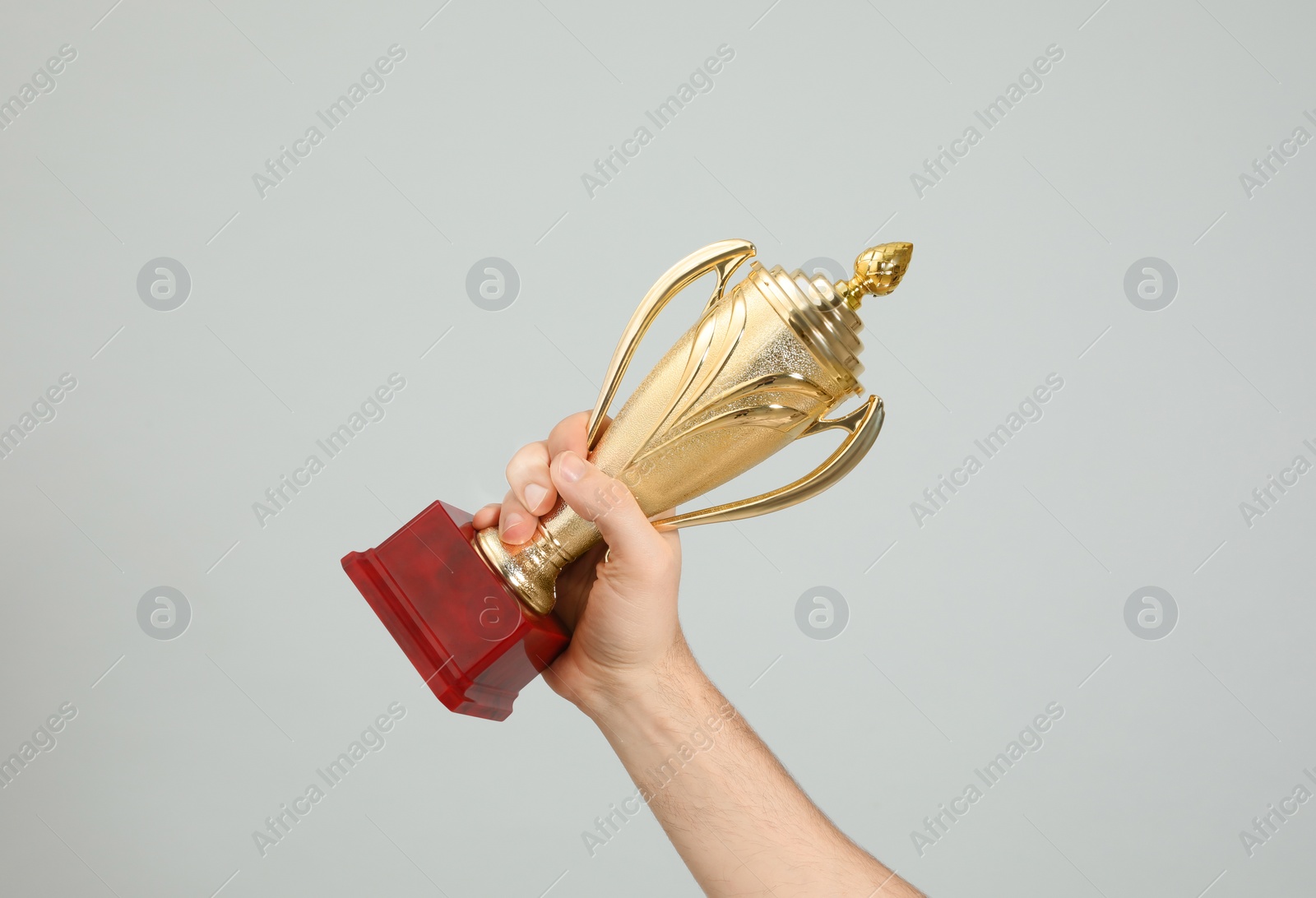 Photo of Man holding gold trophy cup on light grey background, closeup