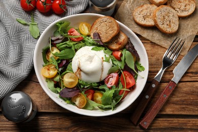 Photo of Delicious burrata salad with colorful cherry tomatoes, croutons and arugula served on wooden table, flat lay