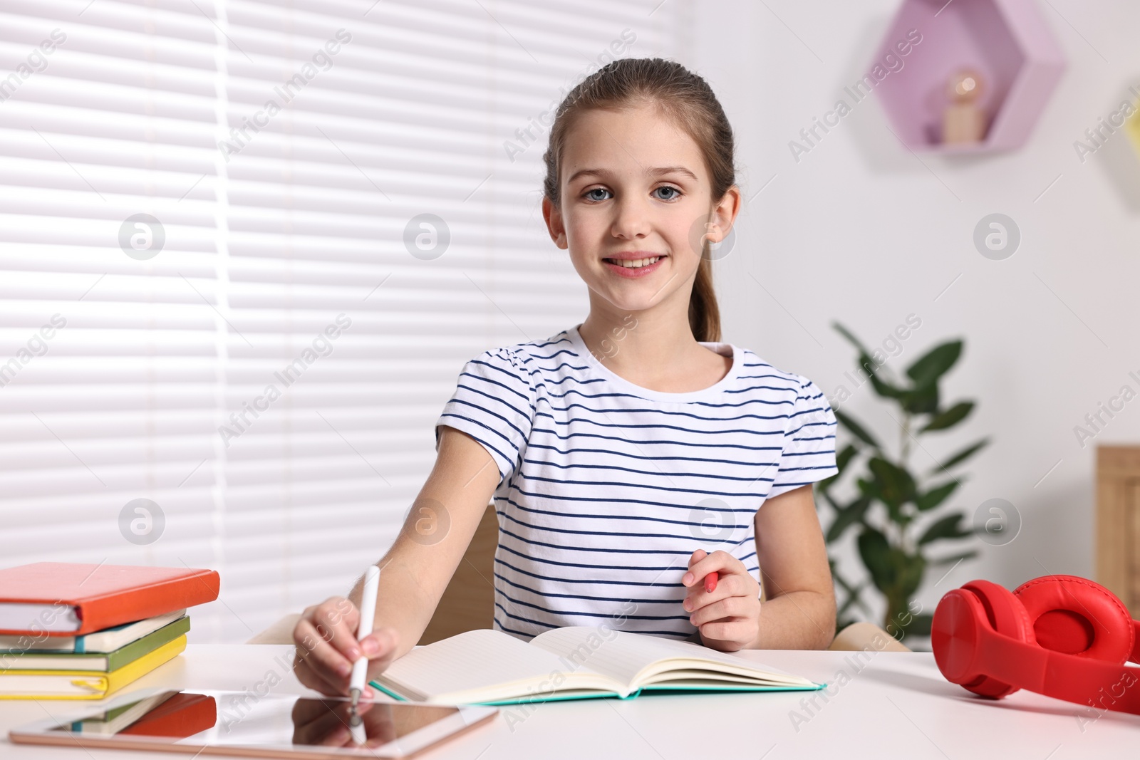 Photo of E-learning. Cute girl using tablet for studying online at table indoors