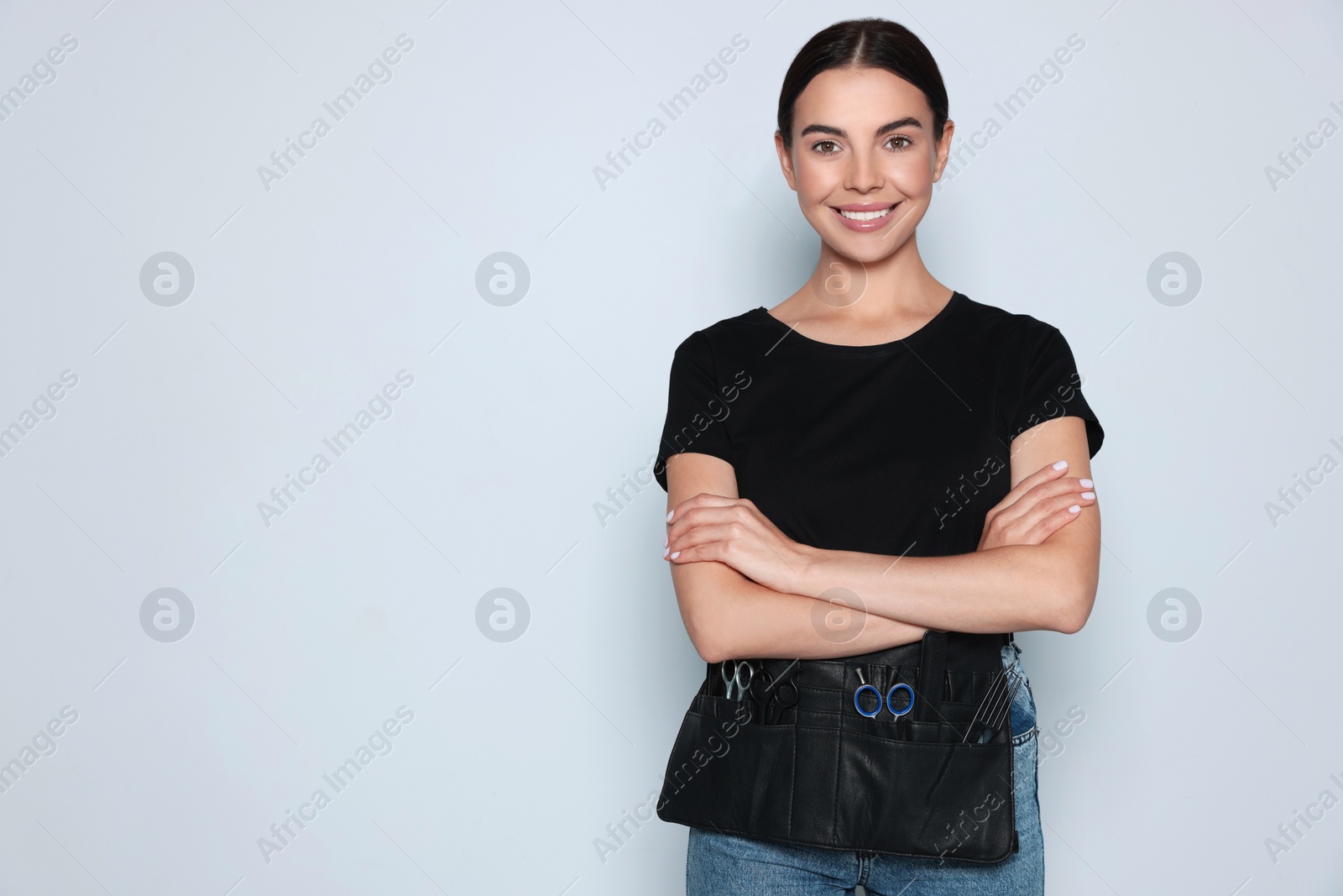 Photo of Portrait of happy hairdresser with professional tools on light background, space for text