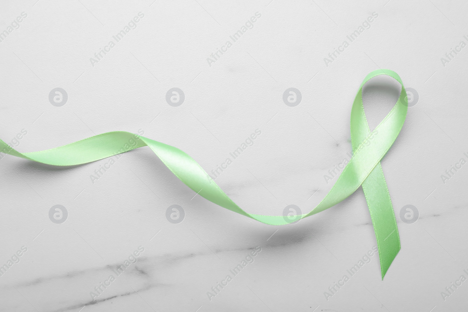 Photo of World Mental Health Day. Green ribbon on white marble table, top view