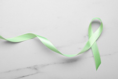 World Mental Health Day. Green ribbon on white marble table, top view