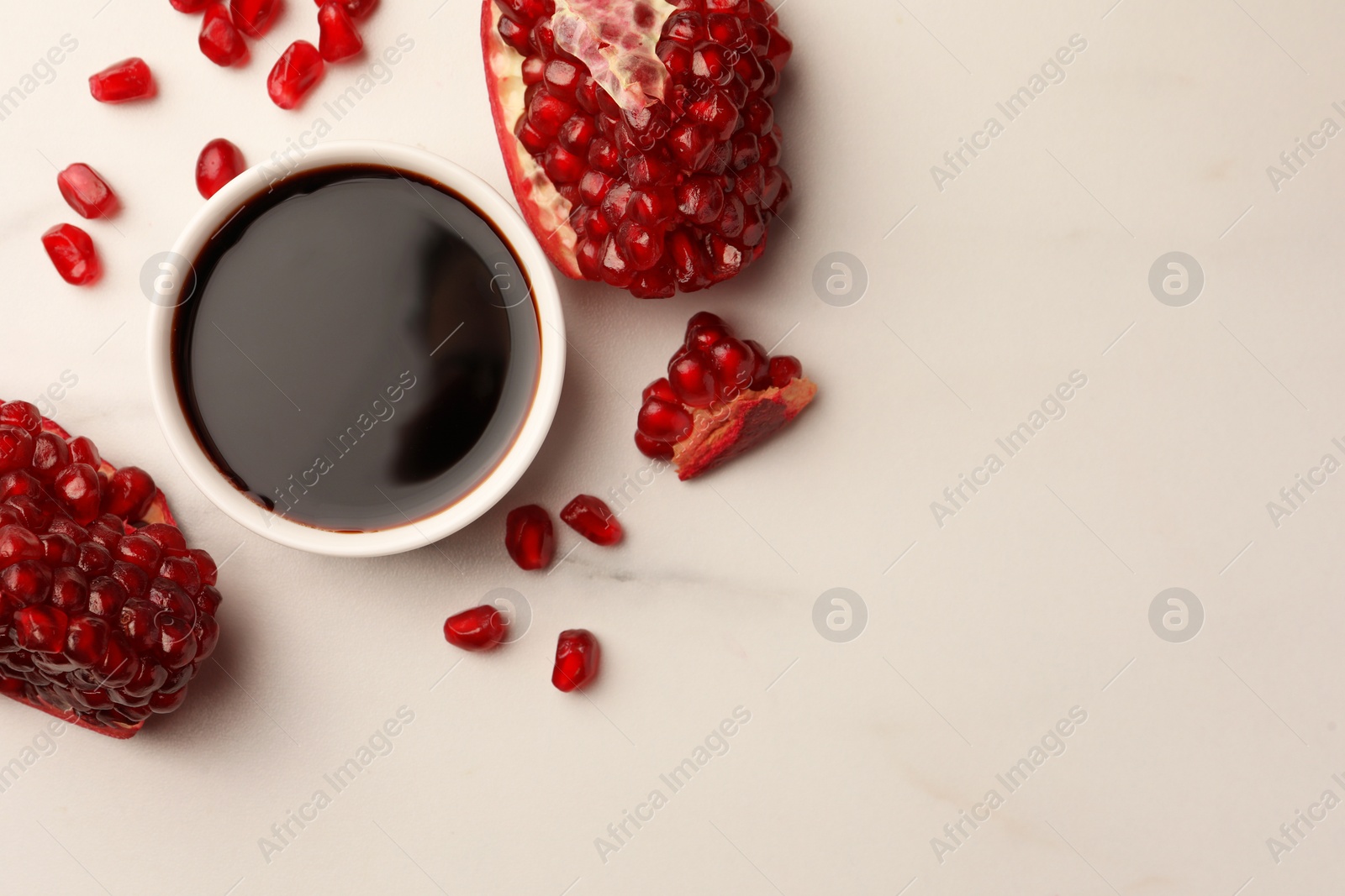 Photo of Bowl of pomegranate sauce and fresh ripe fruit on white marble table, flat lay. Space for text