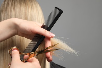 Photo of Hairdresser cutting client's hair with scissors on light grey background, closeup. Space for text