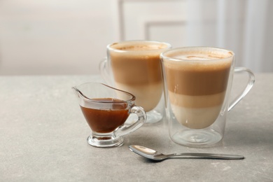 Photo of Glass cups of tasty caramel macchiato and gravy boat with syrup on table