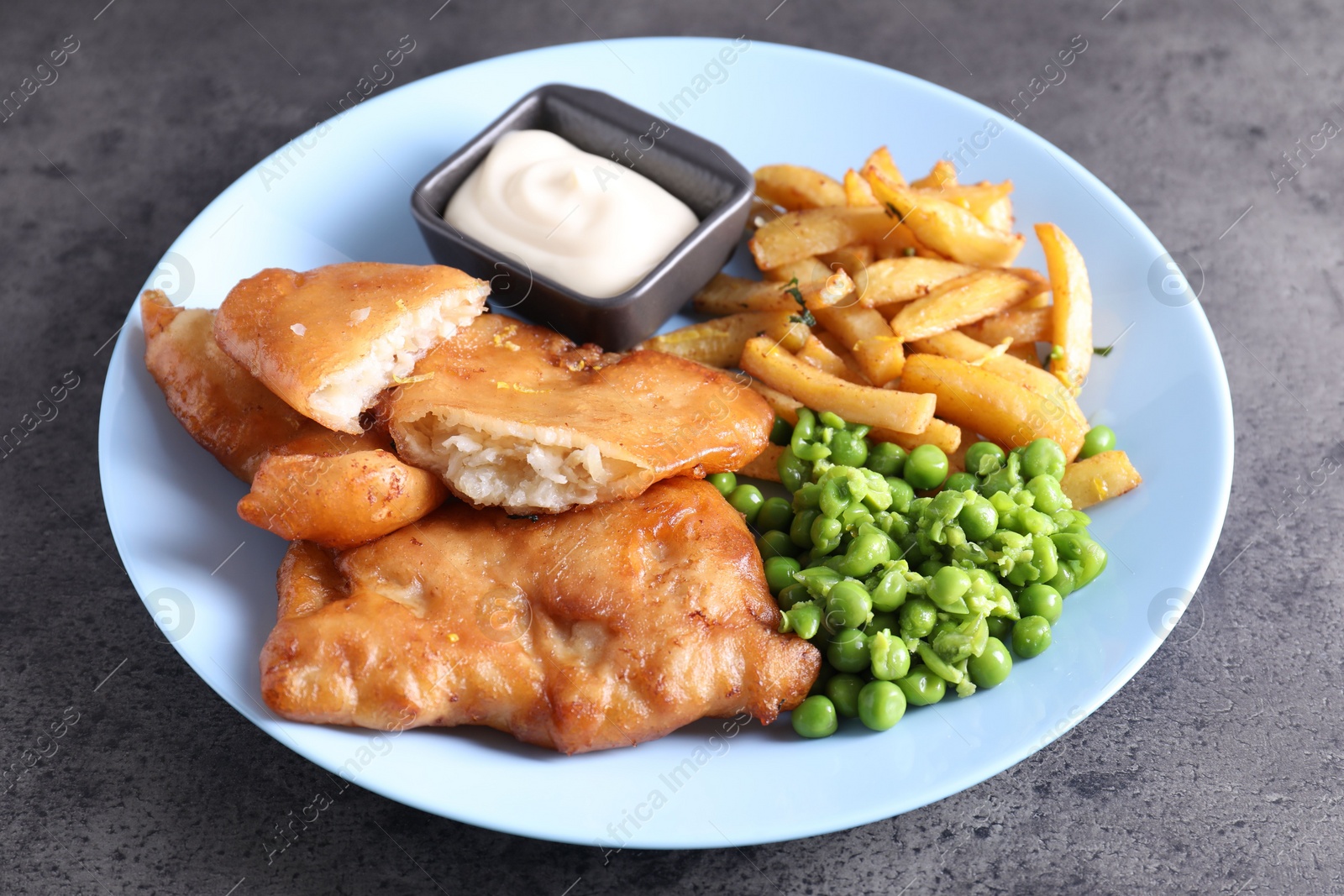 Photo of Tasty fish, chips, sauce and peas on grey table, closeup