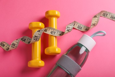 Measuring tape, bottle of water and dumbbells on pink background, flat lay. Weight control concept