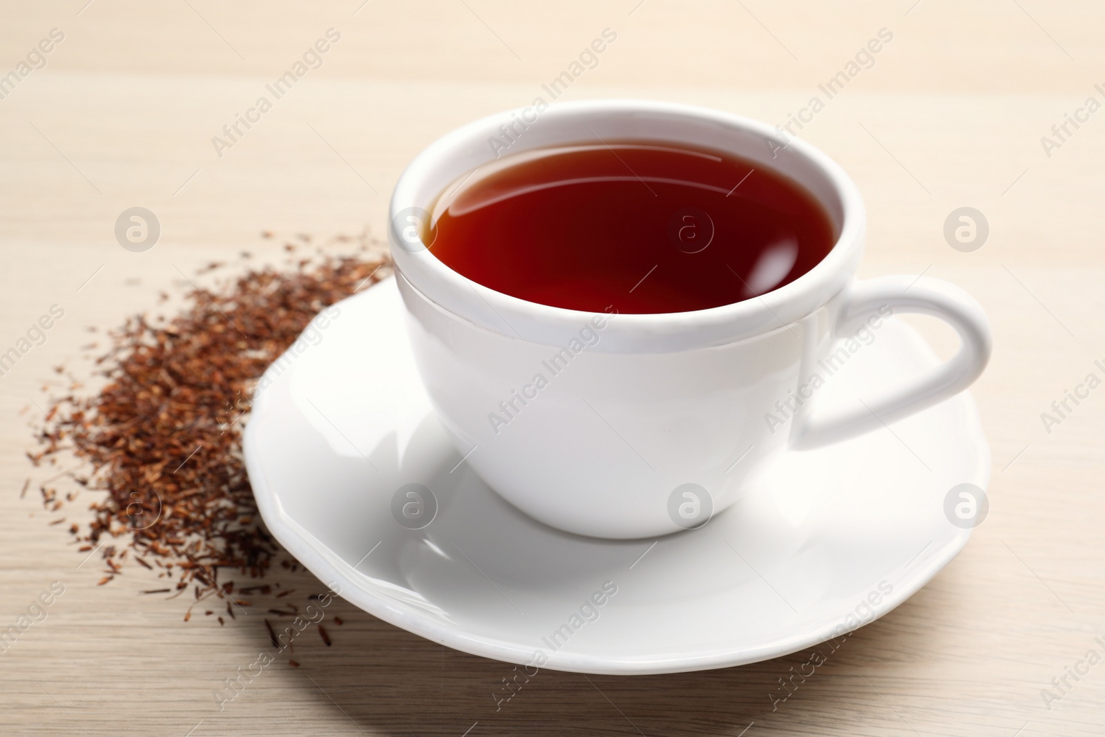 Photo of Freshly brewed rooibos tea and scattered dry leaves on wooden table