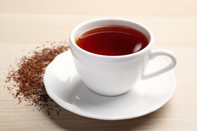 Photo of Freshly brewed rooibos tea and scattered dry leaves on wooden table