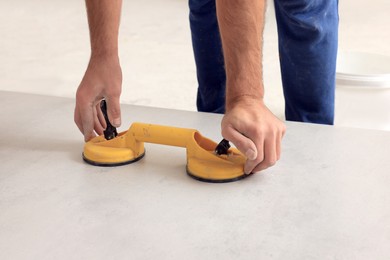 Photo of Worker using suction plate for tile installation indoors, closeup