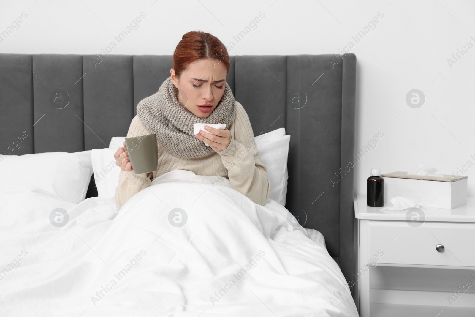 Photo of Woman with cup of drink and tissue coughing at home. Cold symptoms