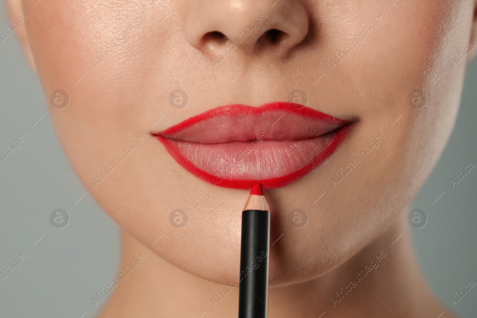 Photo of Young woman applying beautiful red lip pencil on grey background, closeup