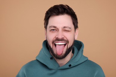 Photo of Happy man showing his tongue on beige background