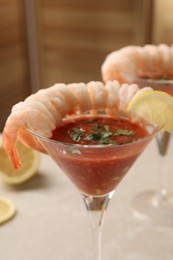 Photo of Tasty shrimp cocktail with sauce in glasses and lemon on light table, closeup