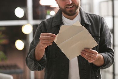 Man holding envelope with greeting card indoors, closeup