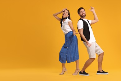 Photo of Happy couple dancing together on orange background, space for text