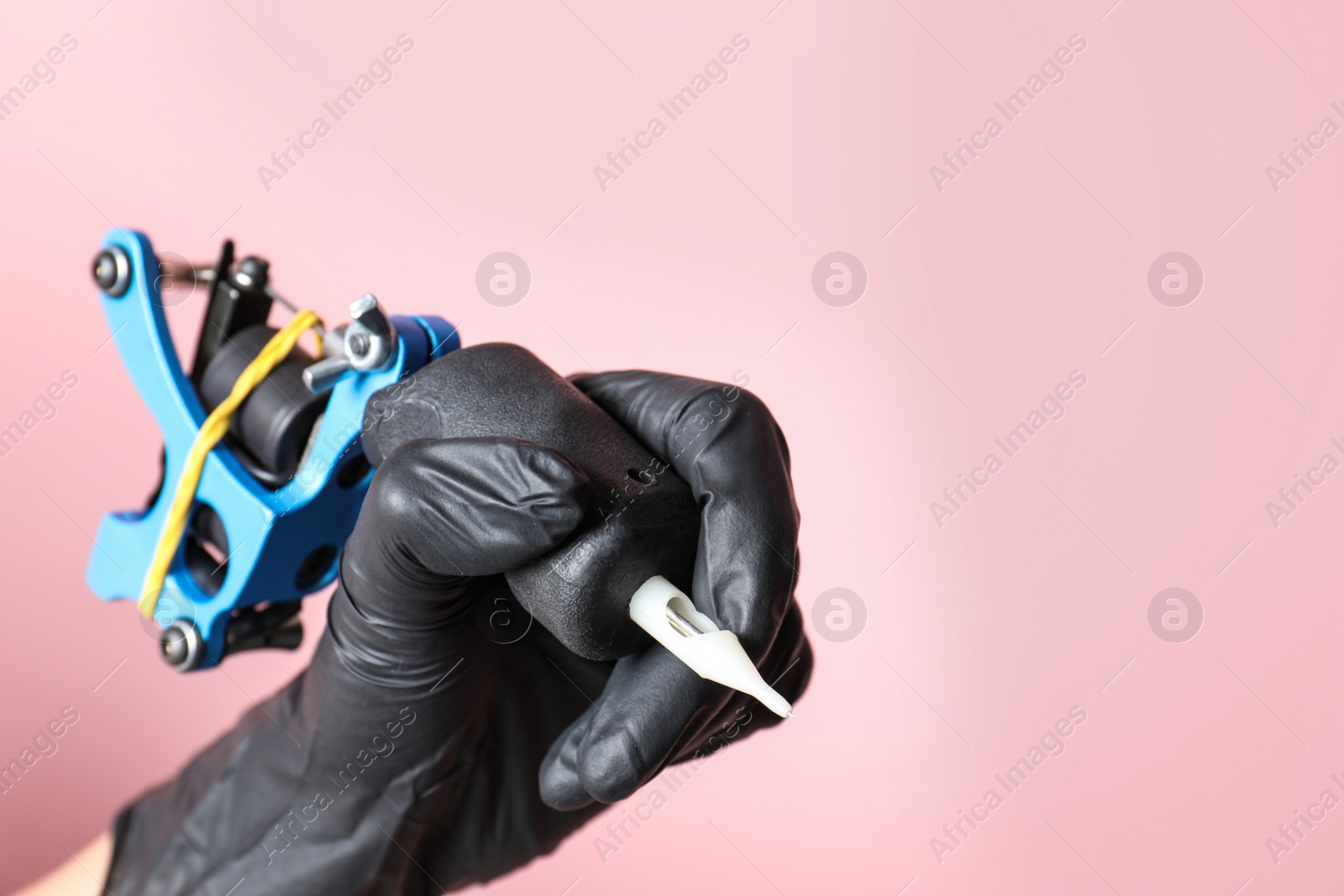 Photo of Professional tattoo artist with machine on color background, closeup. Space for text