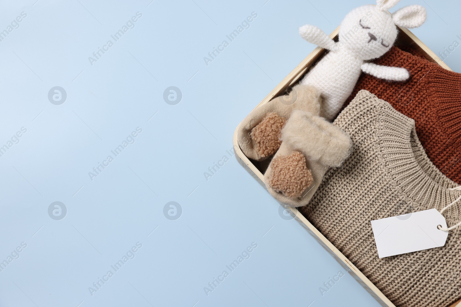 Photo of Different baby accessories, knitted sweaters and blank card in box on light blue background, top view. Space for text