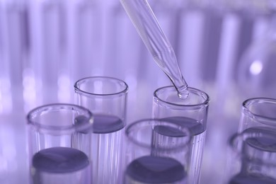 Dripping liquid from pipette into test tube on violet background, closeup