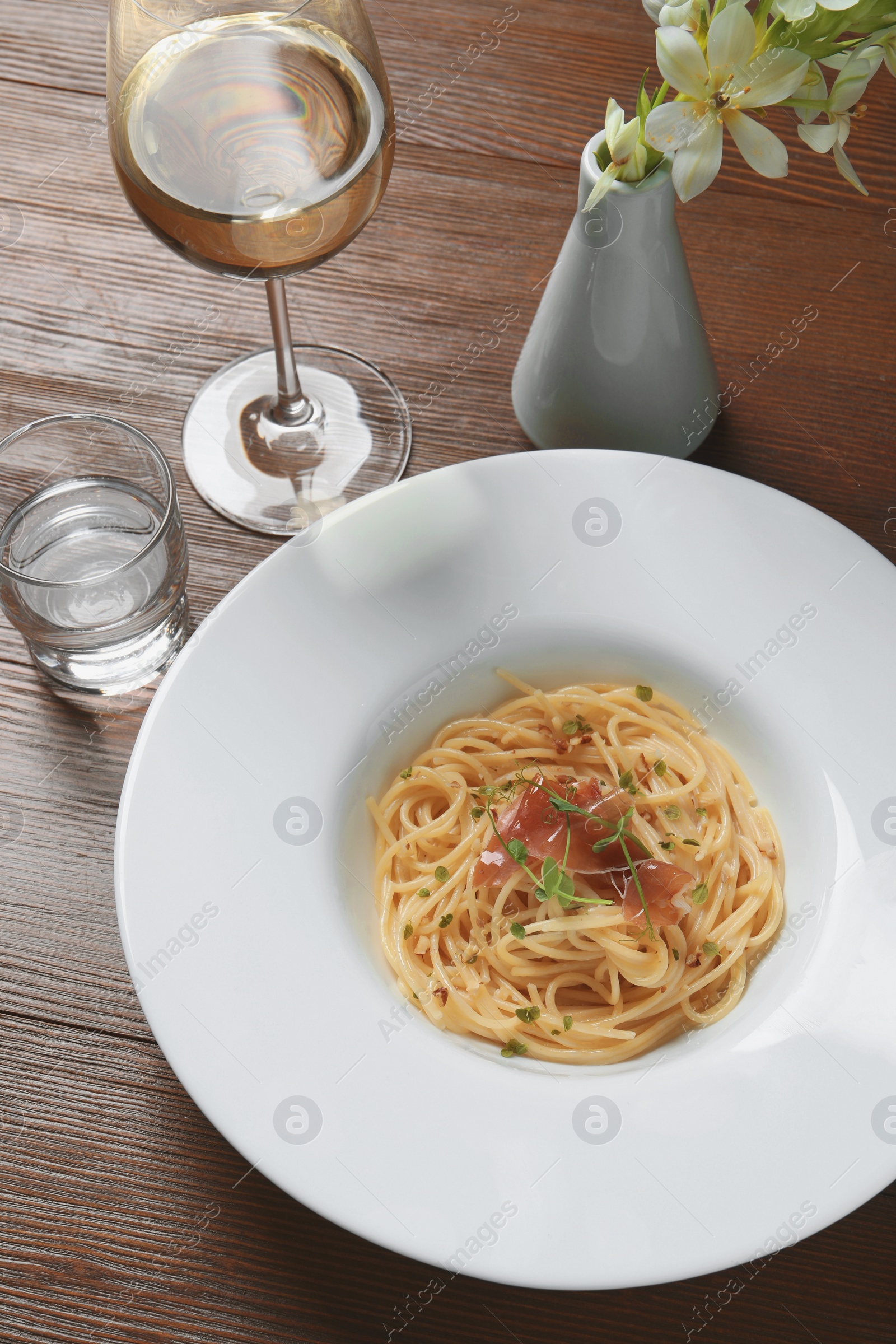 Photo of Tasty spaghetti with prosciutto and microgreens served on wooden table, above view. Exquisite presentation of pasta dish