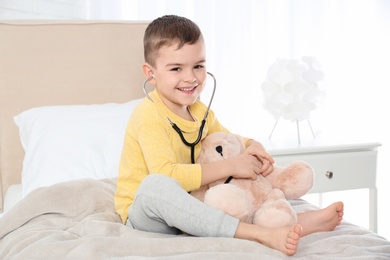 Cute child playing doctor with stuffed toy at hospital