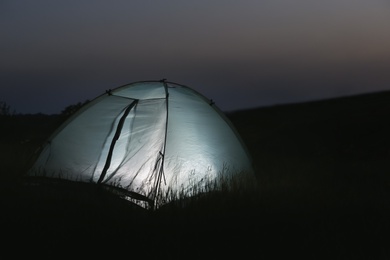 Photo of Modern tent lit from inside in wilderness at night, space for text. Overnight camping