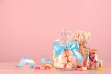 Photo of Jars with different delicious candies on pink wooden table, space for text