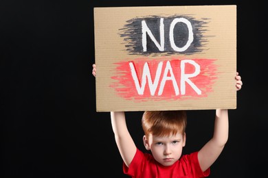 Boy holding poster No War against black background, space for text