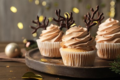 Photo of Tasty Christmas cupcakes with chocolate reindeer antlers on wooden tray, closeup