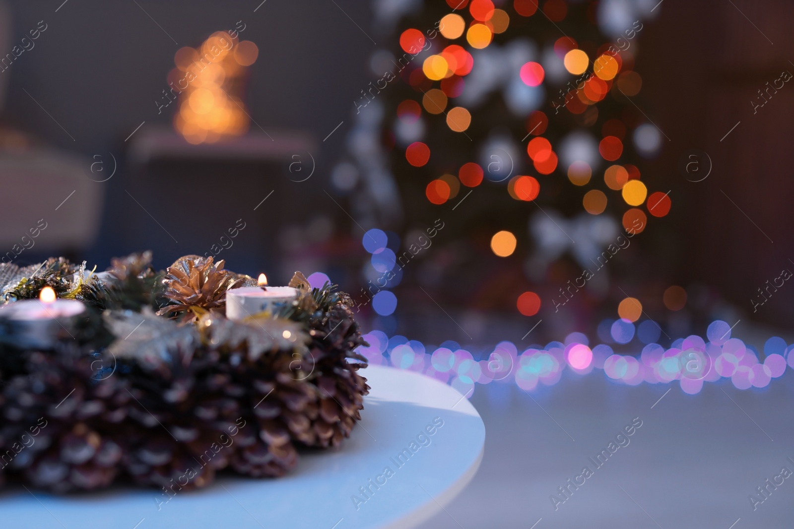 Photo of Beautiful wreath with pine cones on table and Christmas tree in dark room