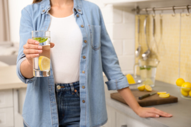 Photo of Young woman with glass of lemon water in kitchen, closeup. Space for text