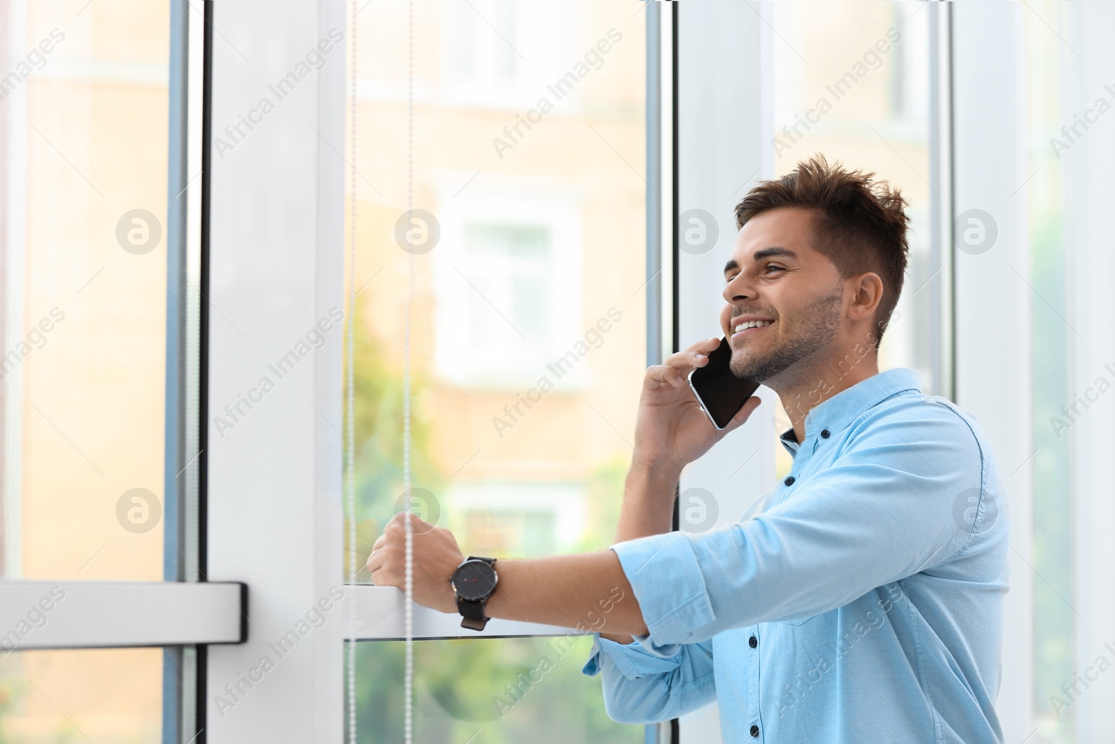 Photo of Portrait of handsome young man talking on mobile phone near window