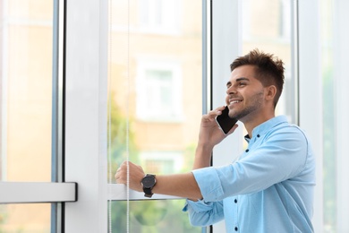 Portrait of handsome young man talking on mobile phone near window