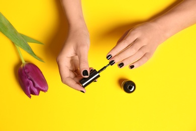 Woman applying nail polish at flower on color background, closeup