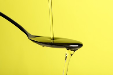Photo of Pouring cooking oil into spoon on yellow background, closeup