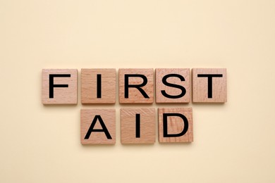 Photo of Words First Aid made of wooden cubes on beige background, flat lay
