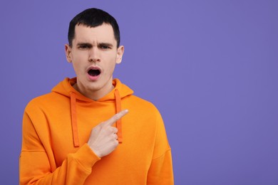 Photo of Surprised man pointing at something on purple background, space for text